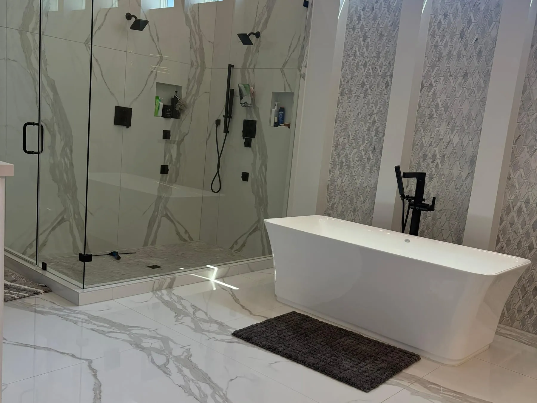 Primary bathroom with a freestanding tub and a marble-tiled walk-in shower, the polished floor reflecting the light
