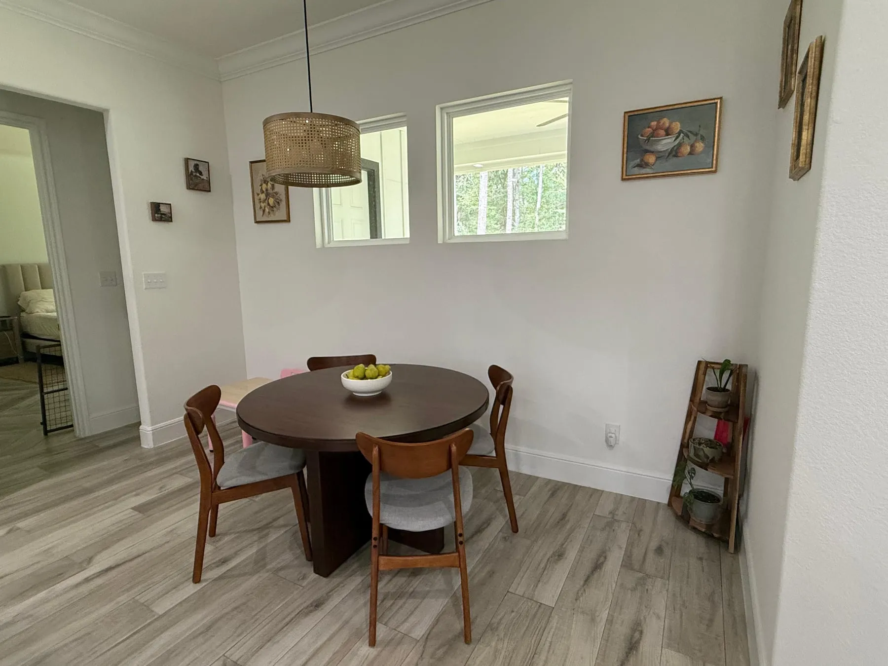 Breakfast nook with a round walnut table and four wooden chairs under a rattan pendant, the table cleared to a bowl of pears and the floor and baseboards clean