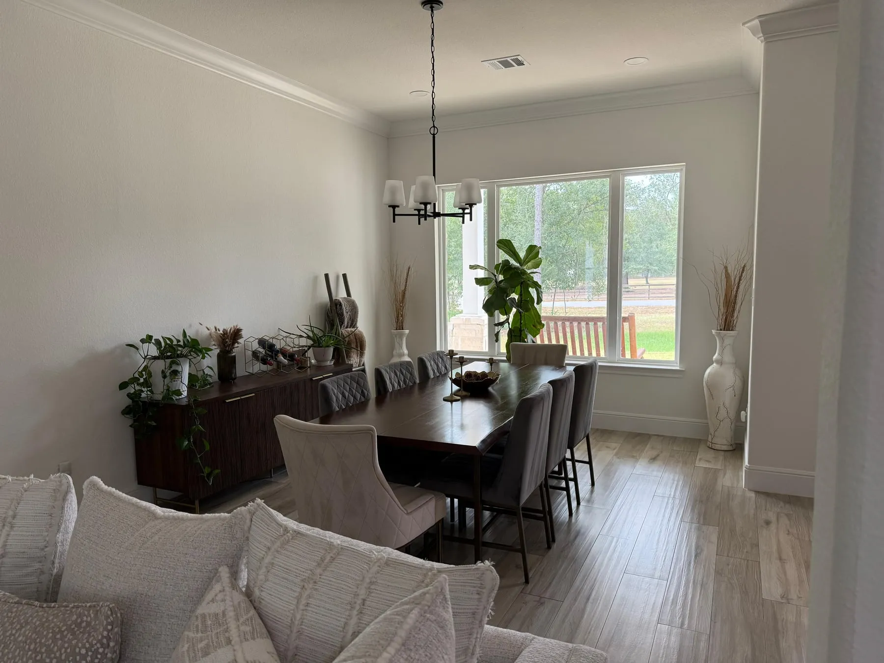 Formal dining room with a long dark wood table and upholstered chairs pushed in, the sideboard dusted and the floor clean to the window