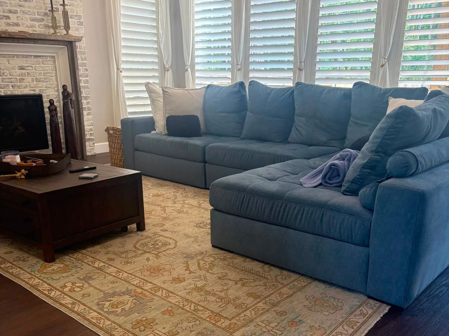 Family room with a blue sectional, cushions plumped and straightened, patterned rug vacuumed and hardwood floor clean