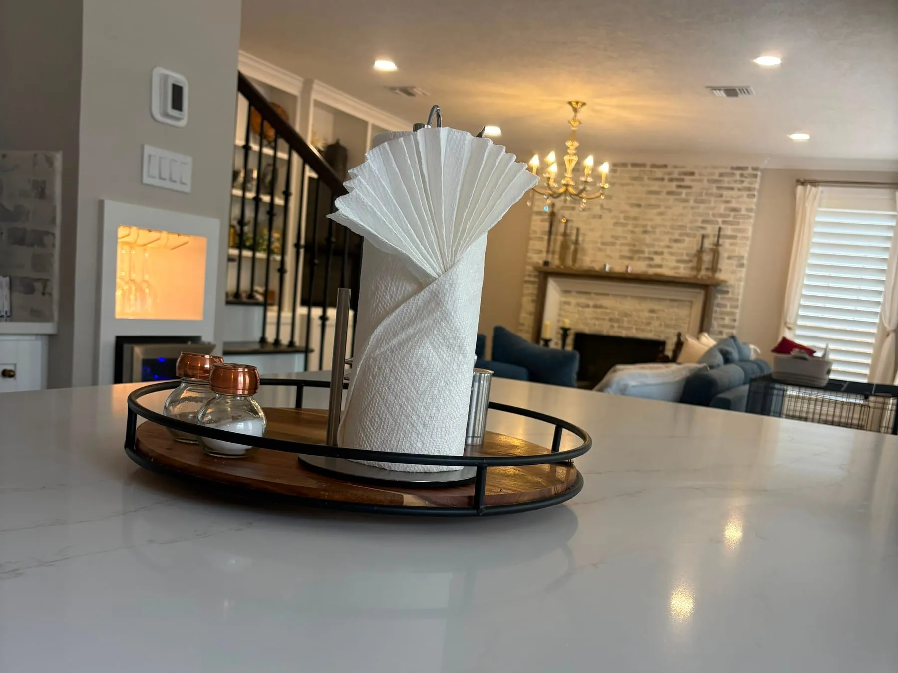 Polished quartz island reflecting the ceiling lights, a folded paper towel on a wooden tray, the living room beyond