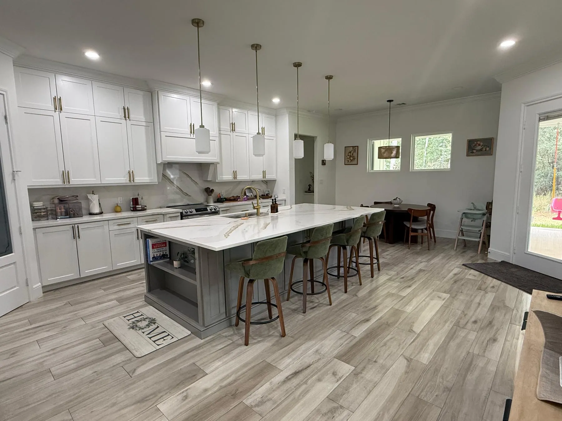 Kitchen with white shaker cabinets and a marble-topped island wiped down, brass tap and green velvet barstools in place, tile floor clean