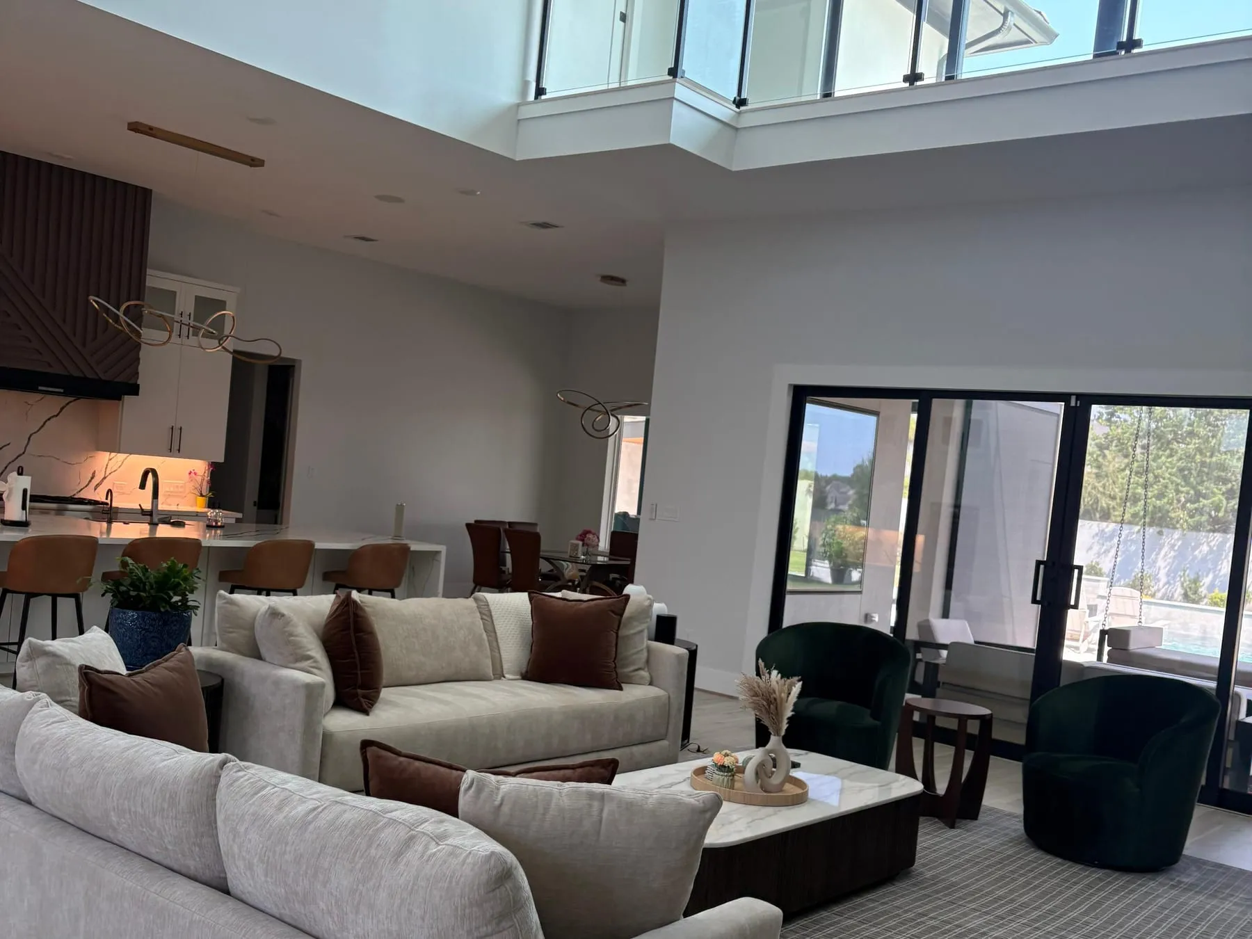 Double-height open-plan living room cleaned and reset, cushions straightened and floors clear, with the kitchen and patio doors beyond