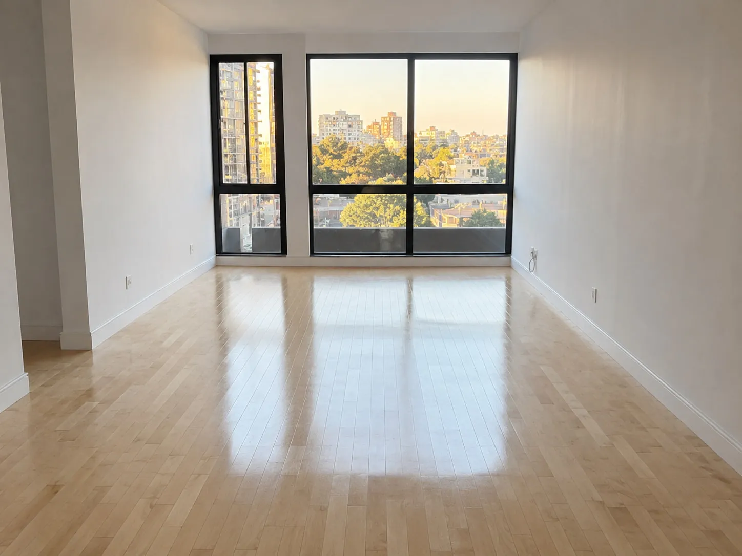 An empty apartment with a freshly cleaned hardwood floor and afternoon light coming through floor-to-ceiling windows