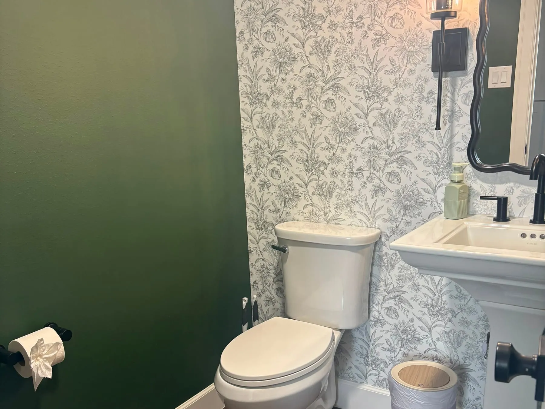Powder room with floral wallpaper and a pedestal sink, fixtures polished and the toilet roll folded to a point