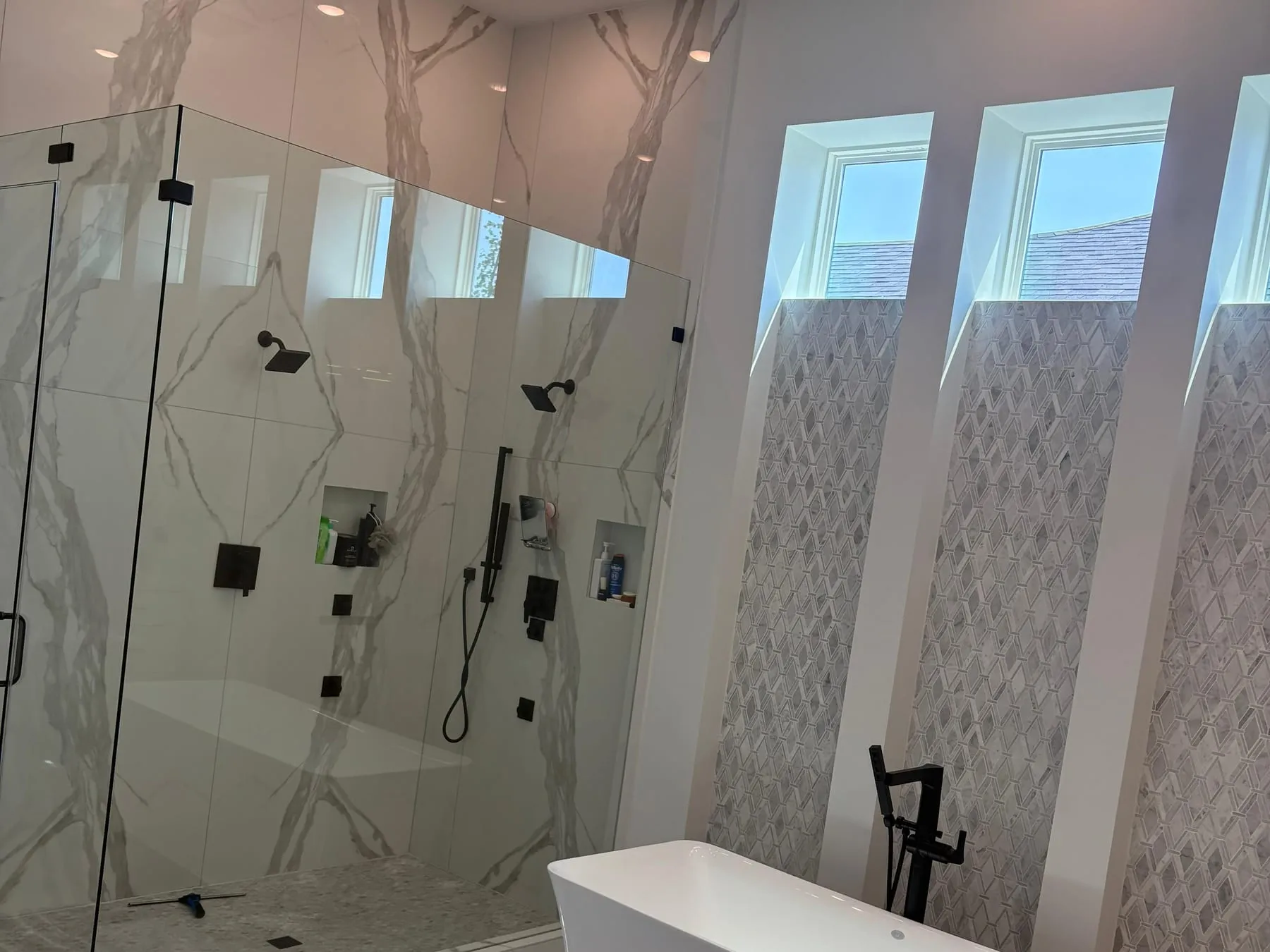 Walk-in shower with streak-free glass panels and marble-look tile, fixtures free of water marks